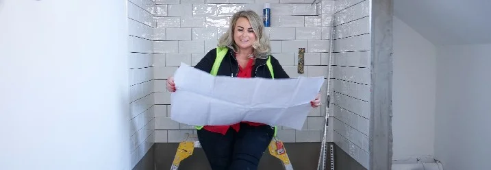 Person betrachtet Bauplan in einem gefliesten Raum.